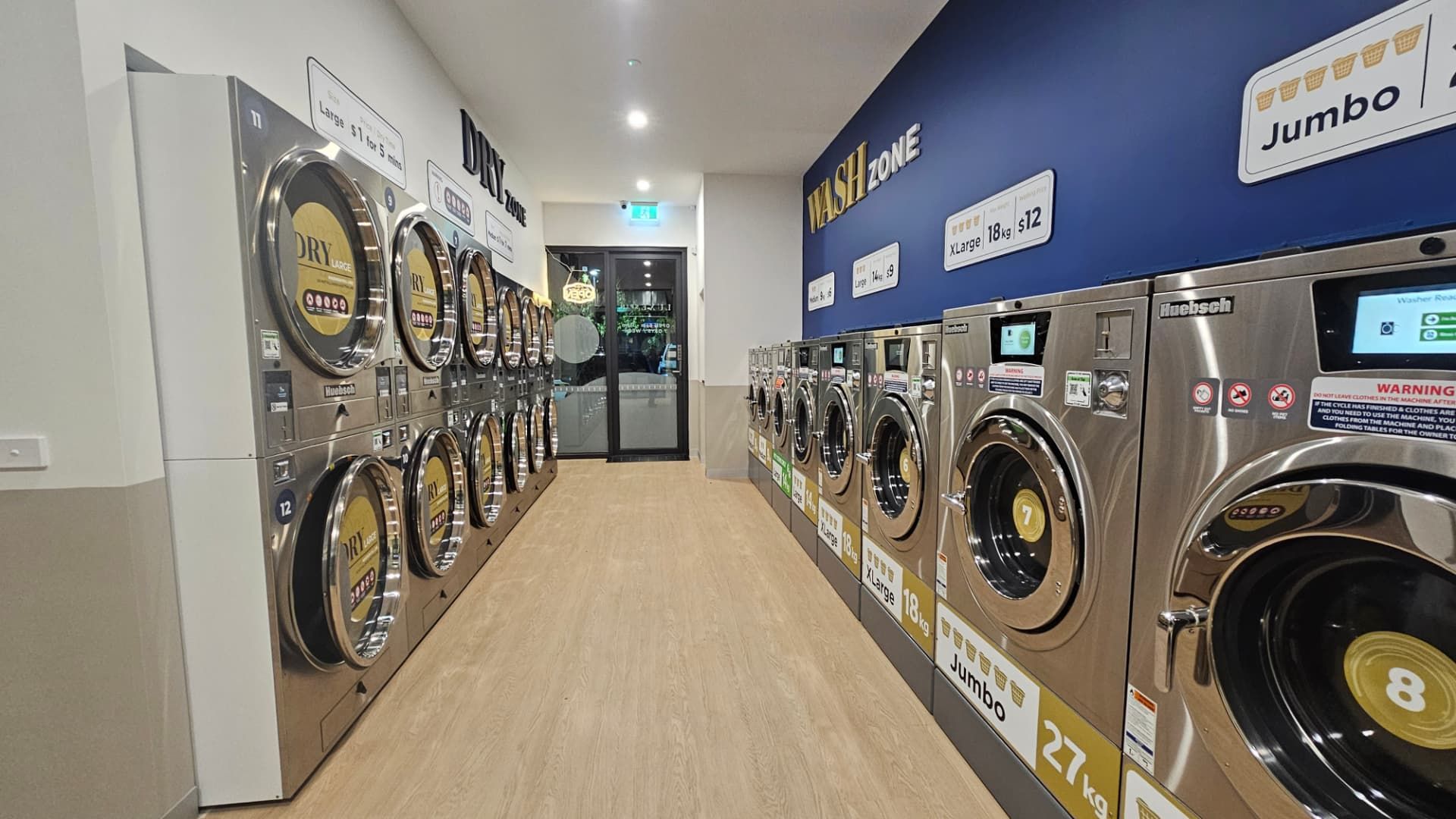 Inside the LuxeSpin laundromat in Officer, showing the Wash Zone commercial washers and the Dry Zone dryers